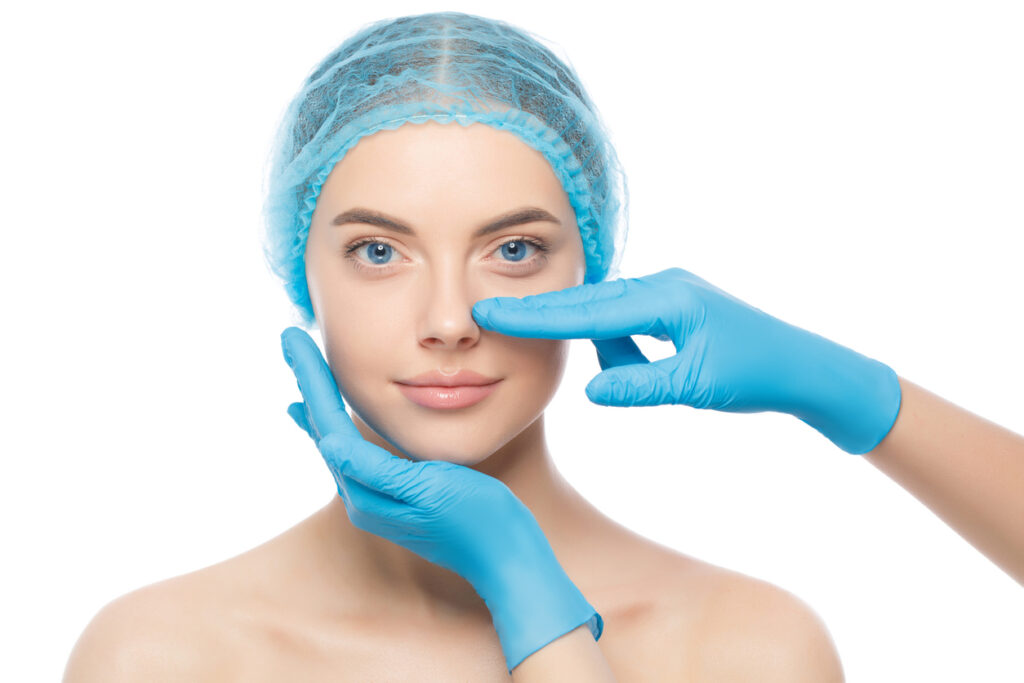 Young woman ready for rhinoplasty, doctor in blue gloves touching her nose