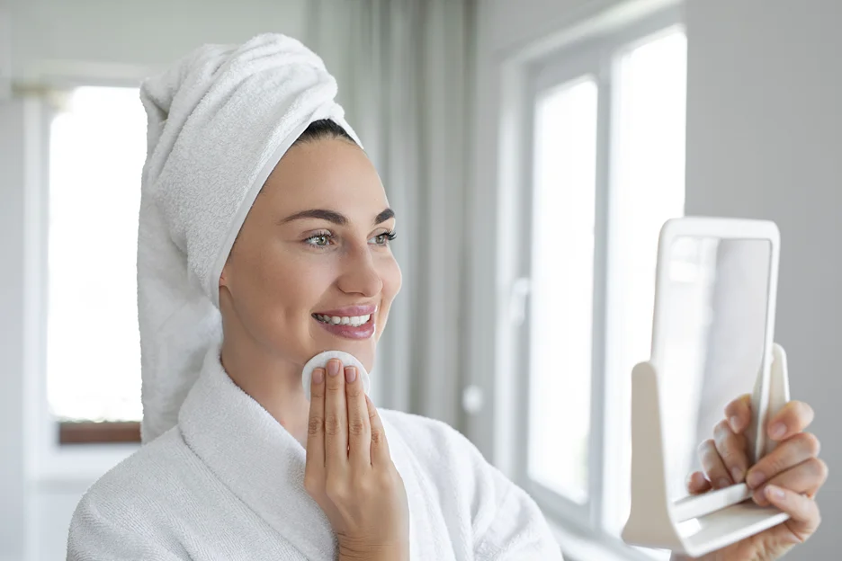 a woman cleanses her face with a facial cleanser infront of the mirror